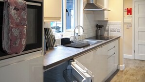 A modern kitchen with a built-in oven, a window, a stainless steel range hood, and a sink with a faucet. - 2 bedroom accommodation in Presteigne (Presteigne)