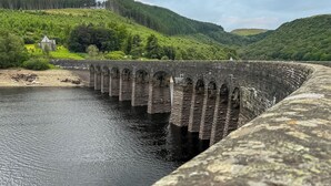 A stone dam with a bridge over a river, surrounded by green hills and a small building. - 2 bedroom accommodation in Presteigne (Presteigne)