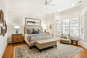 A bedroom with a large bed, two nightstands, a chair, a bench, and a ceiling fan. - 130 Flyway Drive - Villa ESTE - Pool heat optional (Kiawah Island)