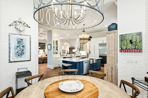 A modern kitchen with white brick walls, a central island, and a chandelier. - 130 Flyway Drive - Villa ESTE - Pool heat optional (Kiawah Island)