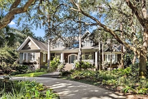 A two-story house with a front porch, surrounded by lush greenery and large trees. - 130 Flyway Drive - Villa ESTE - Pool heat optional (Kiawah Island)