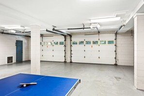 A billiards table with a cue stick and ball, white walls, and garage doors in the background.