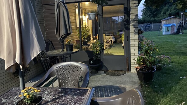 A patio with a table and chairs, a potted plant, and a sliding glass door leading to an interior space with a dining table and chairs.