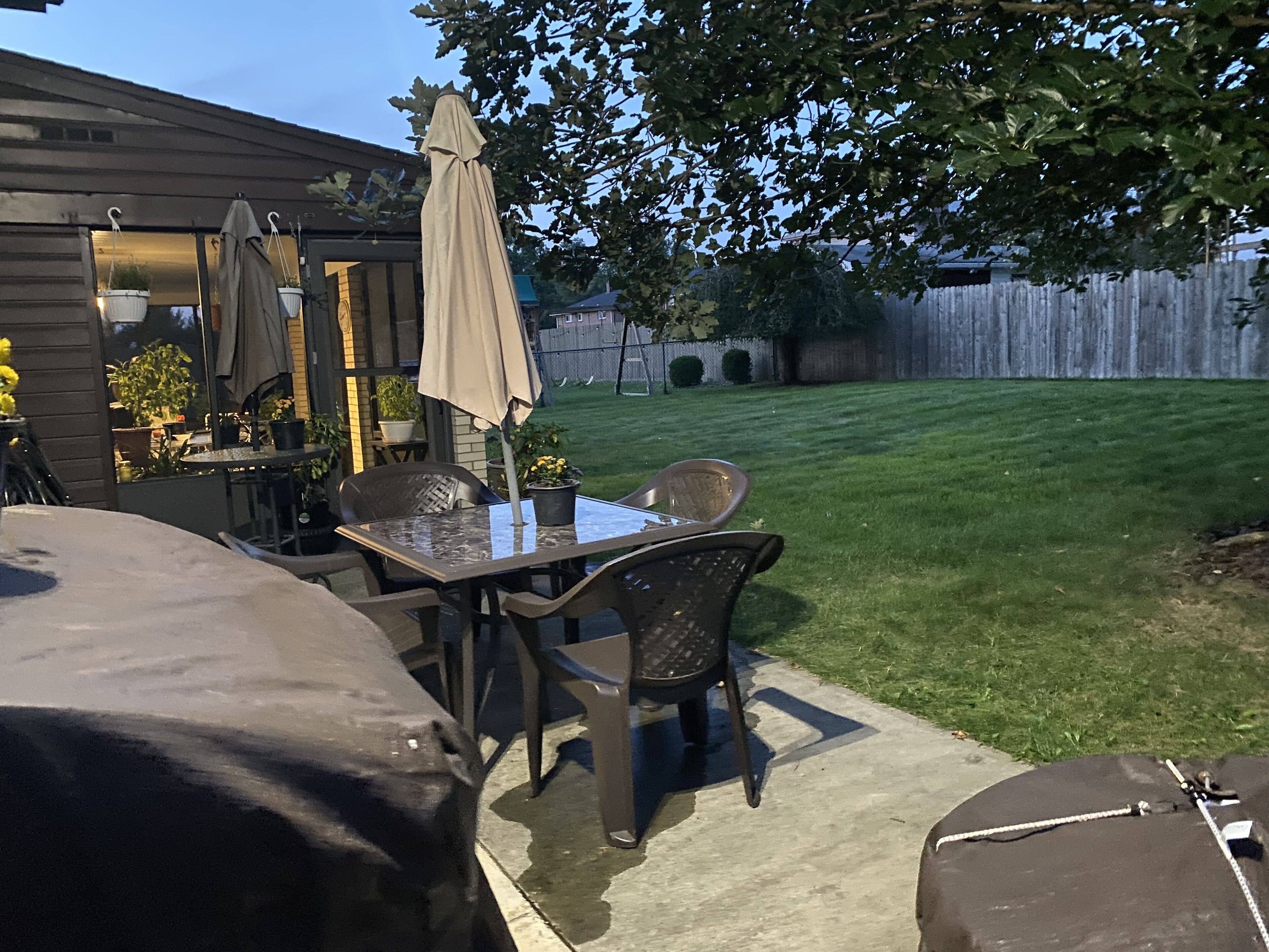 A patio with a table and chairs, a covered umbrella, and a grill.