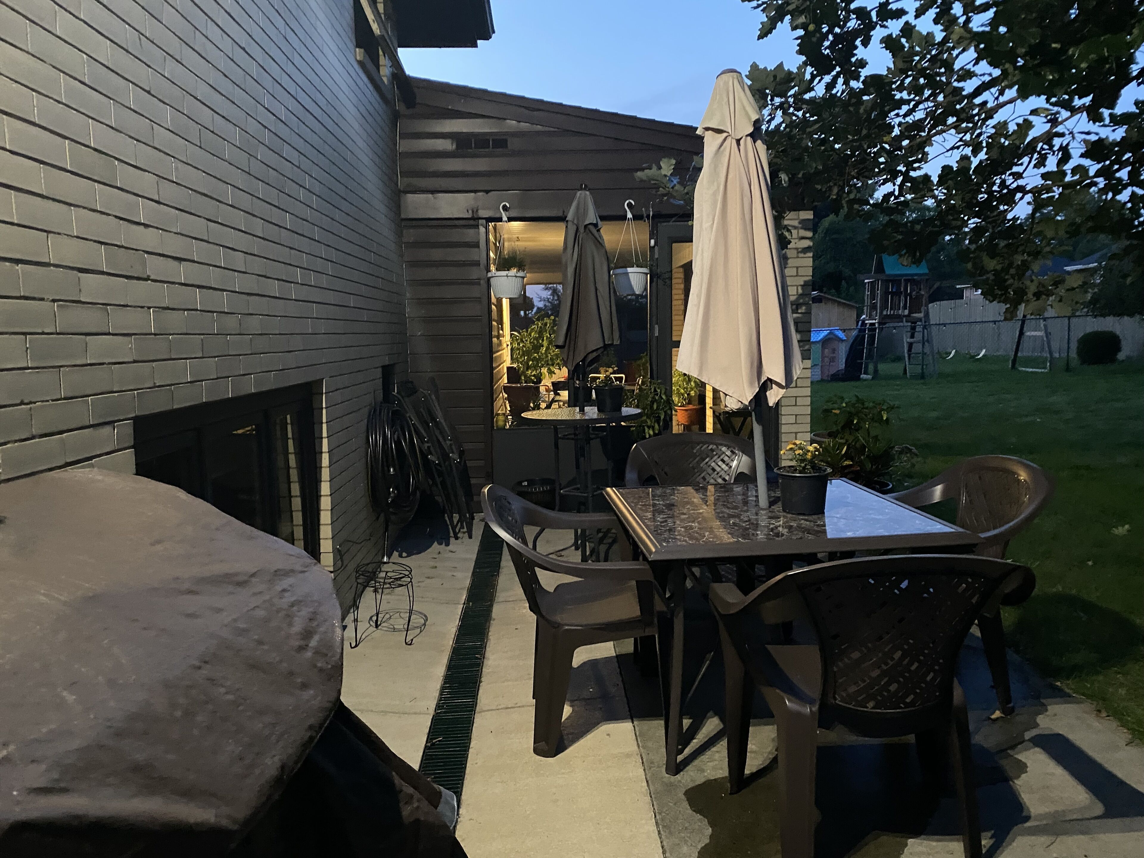 An outdoor patio with a table and chairs, a covered umbrella, and potted plants.