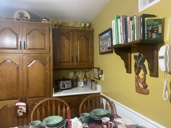A kitchen with wooden cabinets, a dining table with green plates, and a bookshelf with cookbooks.