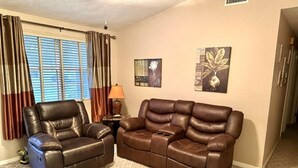 Ein Wohnzimmer mit einem braunen Ledersofa, einem Relaxsessel, einer Lampe und zwei Wandbildern.