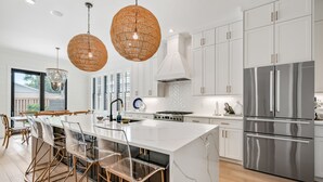 A modern kitchen with white cabinets, stainless steel appliances, and a large island with bar stools. - New Construction - Private Pool - Short Walk to East Beach!  (St. Simons Island)