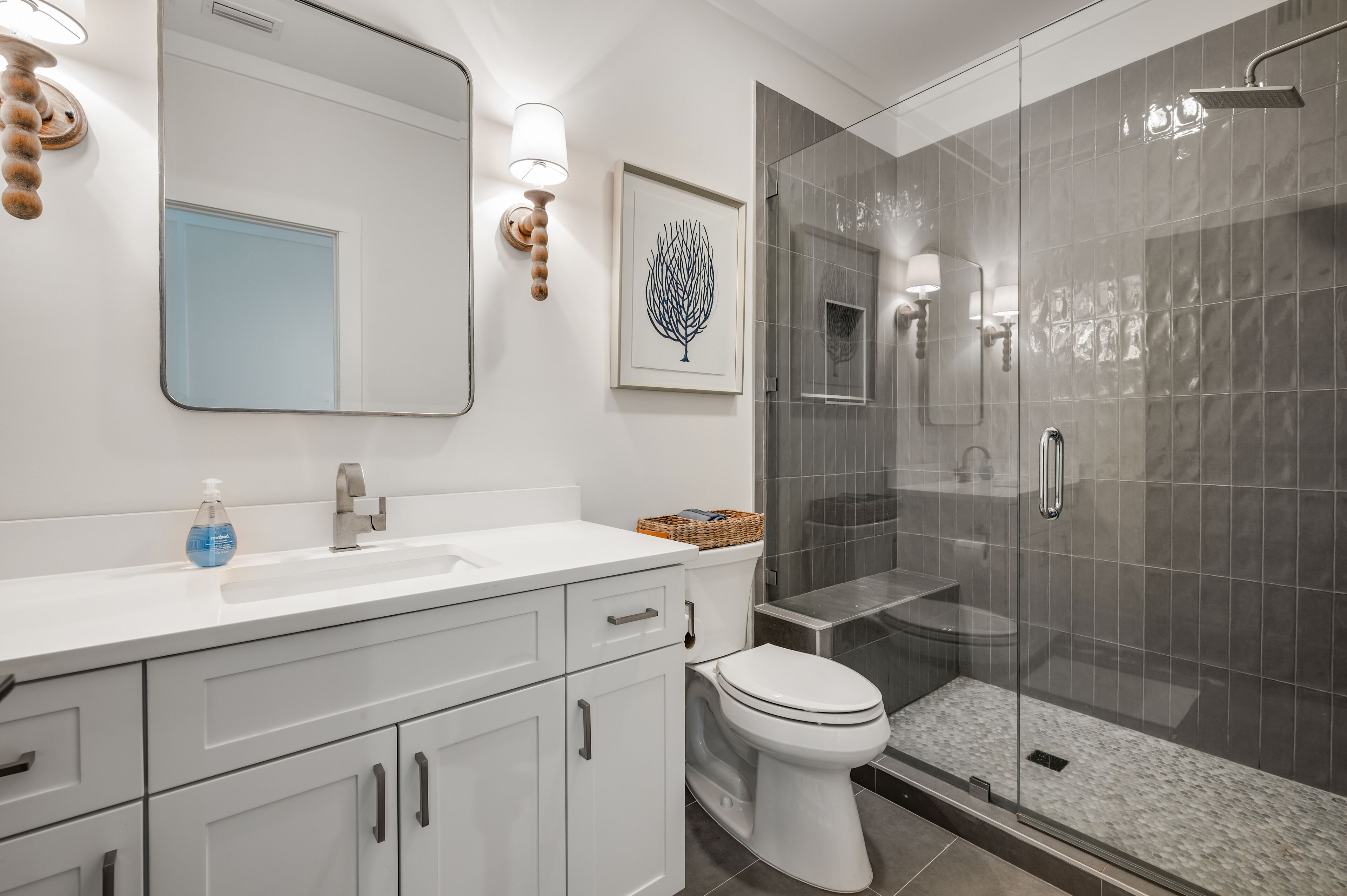A modern bathroom with a white sink, a mirror, a framed artwork, and a glass-enclosed shower area.