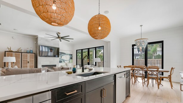 A modern kitchen with a large island, dark cabinetry, and a dining area with wooden furniture. - New Construction - Private Pool - Short Walk to East Beach!  (St. Simons Island)