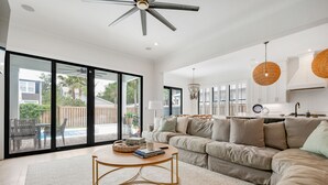 A spacious living room with a large sofa, a coffee table, and a ceiling fan. - New Construction - Private Pool - Short Walk to East Beach!  (St. Simons Island)