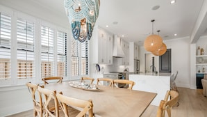 A modern kitchen with white cabinetry, a central island, and wooden chairs around a large table. - New Construction - Private Pool - Short Walk to East Beach!  (St. Simons Island)