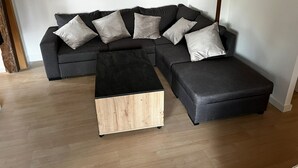 A modern living room with a dark grey sectional sofa, multiple light grey cushions, and a black and light wood coffee table. - 4 Bedroom Apartment in TrÃ©venans (Trévenans)