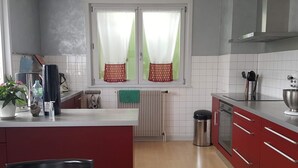 A kitchen with a red countertop, white tiled backsplash, and a window with curtains. - 4 Bedroom Apartment in TrÃ©venans (Trévenans)