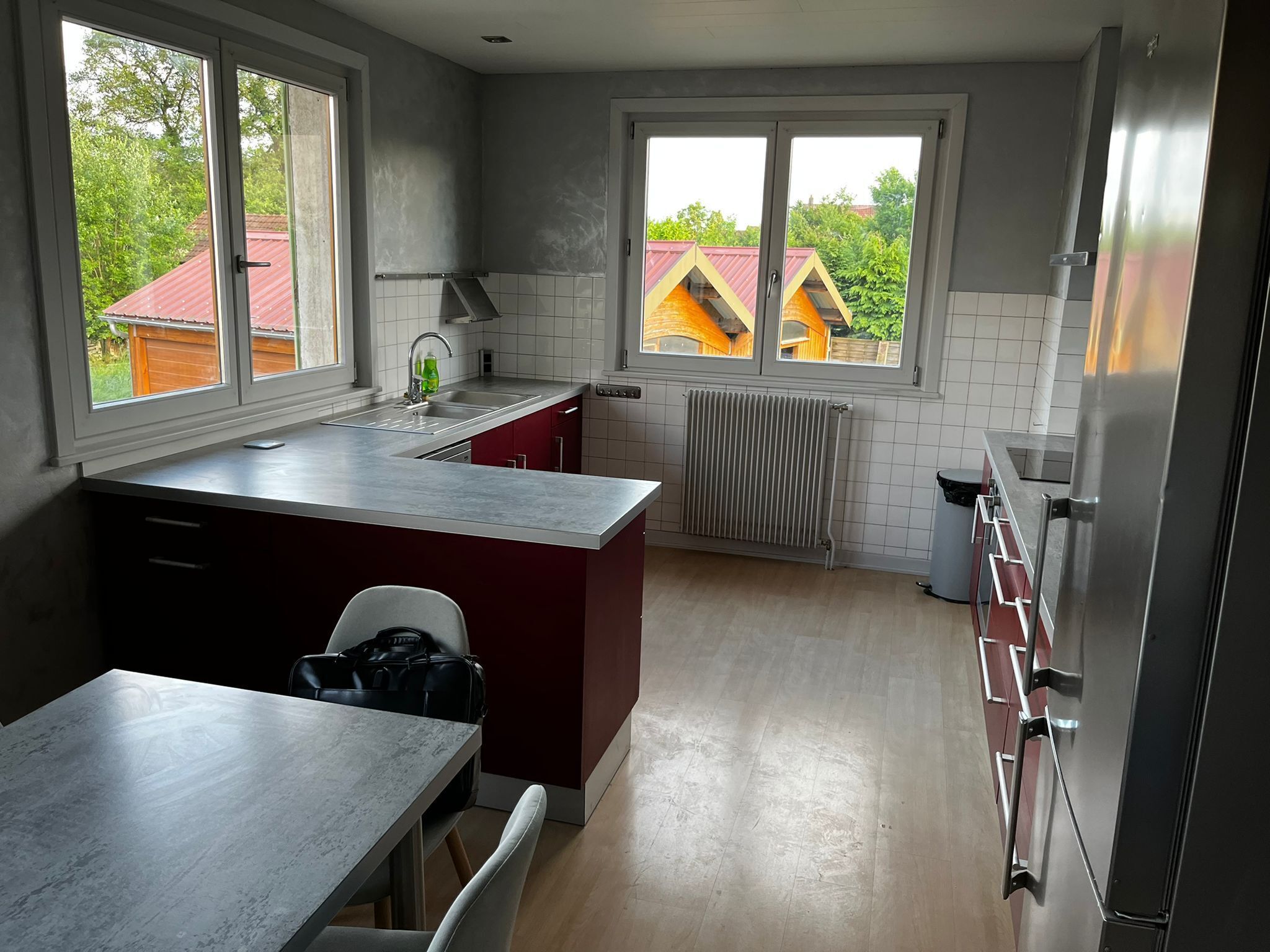 A modern kitchen with a central island, a built-in oven, and a window with a view of houses.