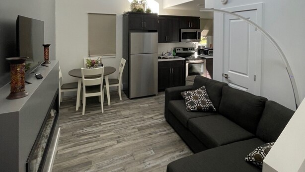 A modern kitchen with dark cabinets, a refrigerator, and a microwave. There is a dining table with chairs and a small plant on the counter. - The Cottages@Gull&Castle#4 (Wasagaming)