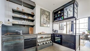 A modern kitchen with dark cabinetry, a built-in oven, and a variety of storage shelves. - The Workshop Near Eiffel Tower by Mon Petit Faré (Paris)