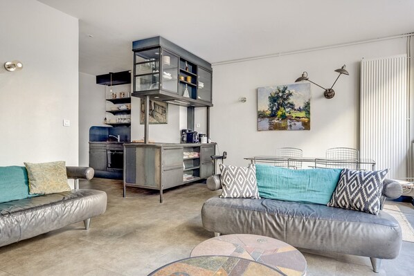 Een moderne woonkamer met een bank, een salontafel en een keukenhoek met een inbouwmeubel.