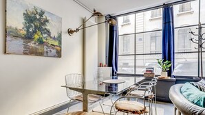 A modern living room with a glass table, metal chairs, a leather sofa, and a large window with curtains. - The Workshop Near Eiffel Tower by Mon Petit Faré (Paris)