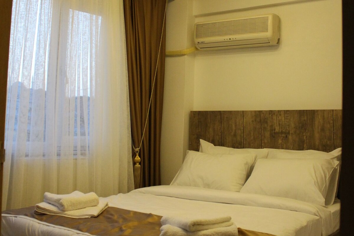 Habitació d'hotel amb un llit, cortines, un aparell d'aire condicionat i una làmpada al sostre.