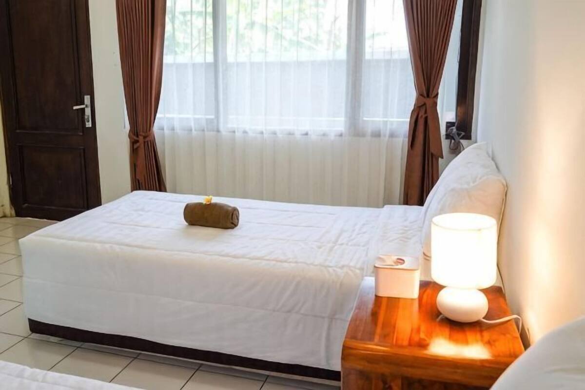 Ein Hotelzimmer mit einem Bett, einem Nachttisch mit Lampe und einem Fenster mit Vorhängen.