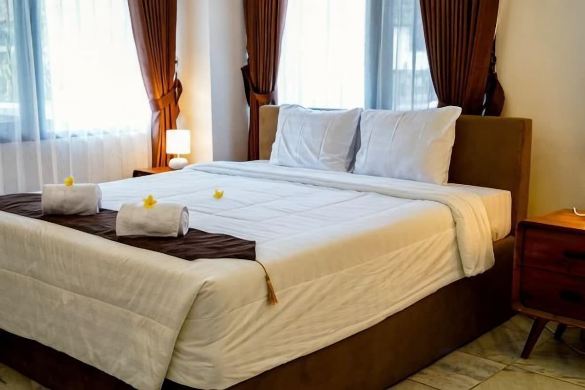 A neatly made bed with a white bedspread, two pillows, and a decorative towel on the side.