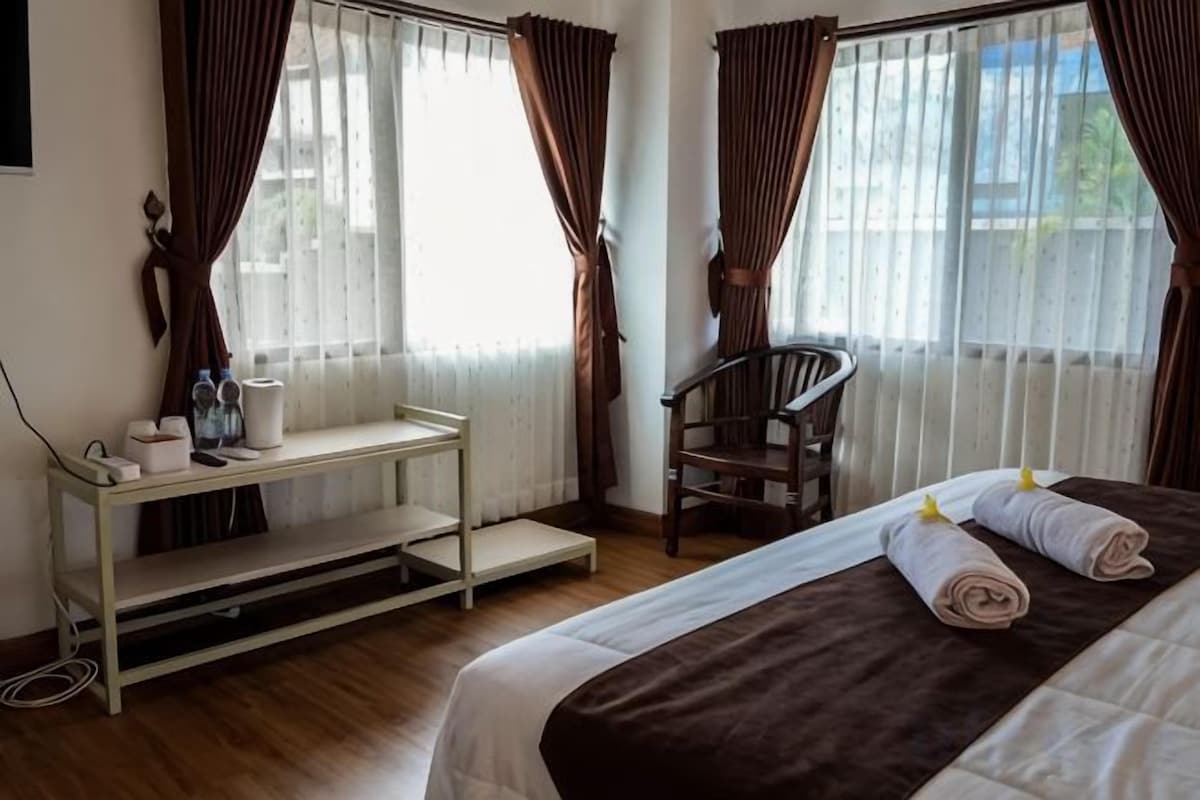 Una habitación de hotel con una cama, una silla, una mesita y cortinas.