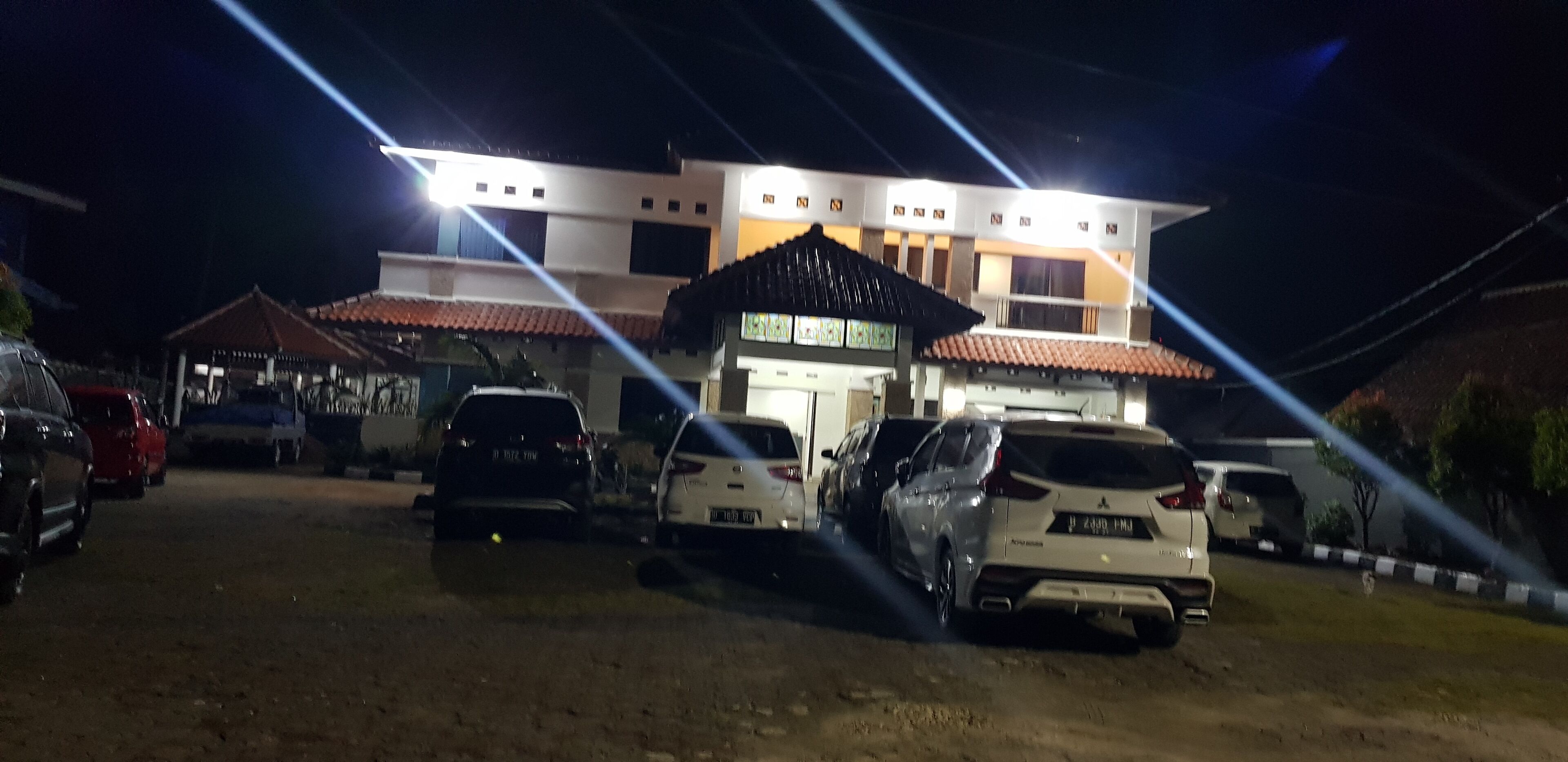 A parking lot with several cars parked in front of a building with multiple floors and a tiled roof.