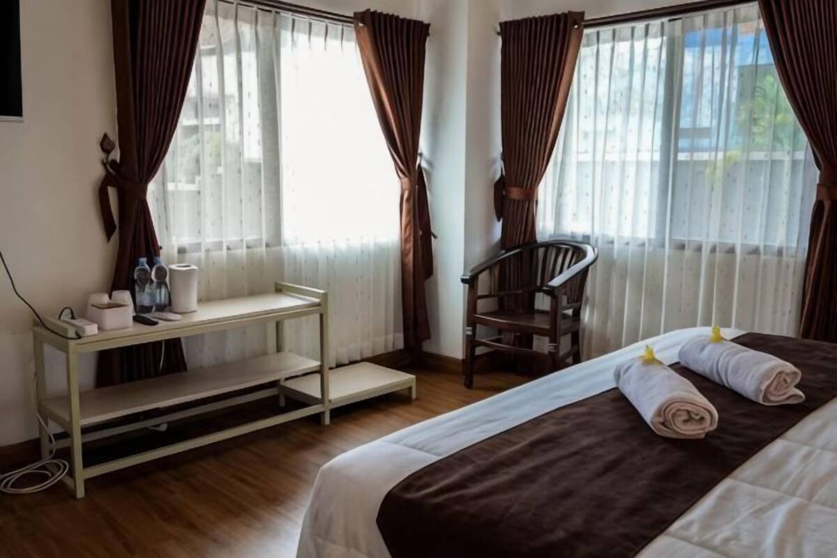 Ein Hotelzimmer mit einem Bett, einem Sessel, einem kleinen Tisch mit Gegenständen und Vorhängen.