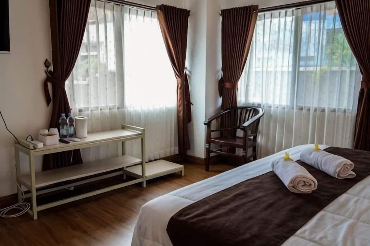 A hotel room with a bed, a chair, a small table with items, and curtains.