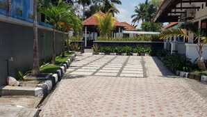 A paved pathway leading to a building with a red-tiled roof, surrounded by greenery and palm trees. - Hotel pondok putri (Cijulang)