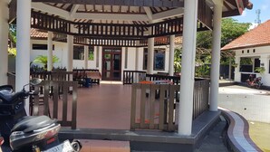 A covered outdoor seating area with wooden benches and tables, a scooter parked in the foreground, and a building with a tiled roof in the background. - Hotel pondok putri (Cijulang)
