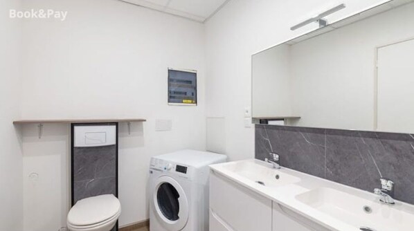 Bathroom features a double sink, toilet, and washing machine.