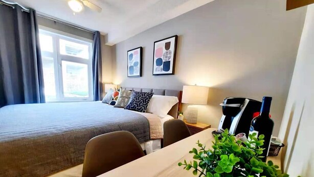 A hotel room with a large bed, a desk with a coffee maker, a wine bottle, and a potted plant. - Enjoy Serenity & Relax in 1BR/BA w/ Mountain View, 10 minutes drive to Banff  (Canmore)