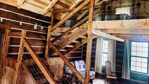 A rustic wooden interior with exposed beams, a loft area, and a view of the outdoors through a window.