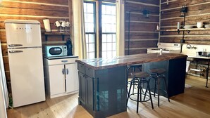 A kitchen with wooden walls, a refrigerator, a microwave, a sink, and a bar area with stools.