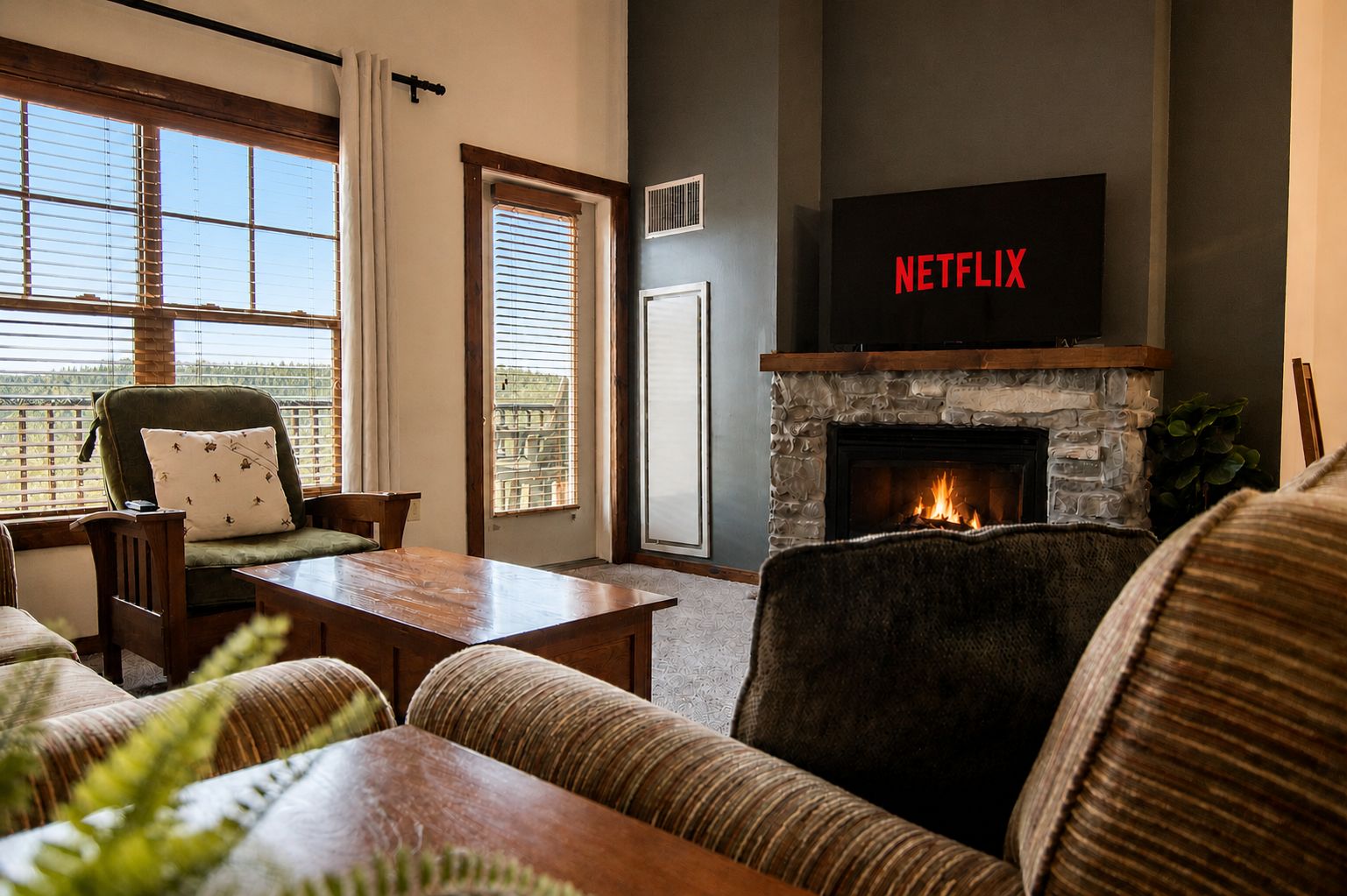 Ein Wohnzimmer mit Kamin, einem darüber hängenden Fernseher und Blick durch das Fenster.