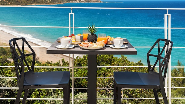 A table with breakfast items and two chairs overlooking a beach and ocean. - Emerald Boutique Hotel (Cefalù)