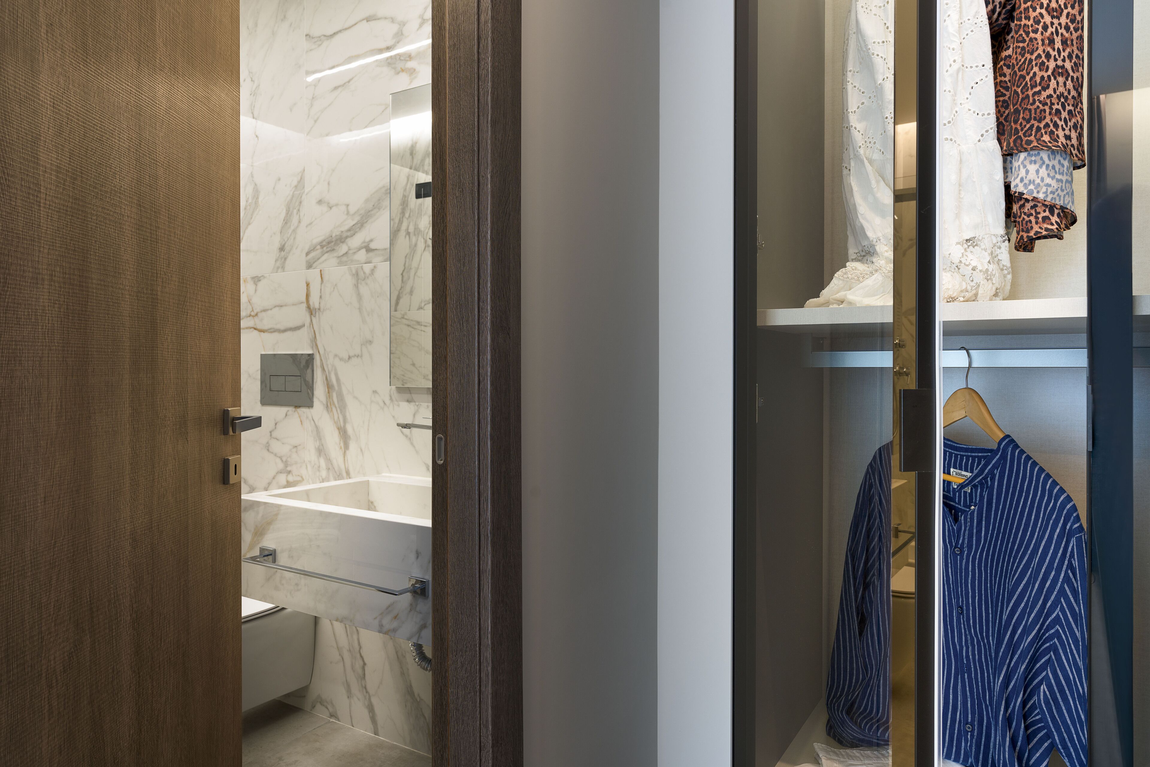 A bathroom with a marble wall, a wooden door, and a hanging robe.
