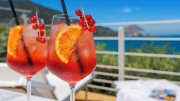 Two glasses of red beverage with orange slices and red berries, set on a balcony with a scenic view.