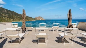 A rooftop pool area with white lounge chairs and umbrellas, overlooking a clear blue sea and a mountainous landscape. - Emerald Boutique Hotel (Cefalù)