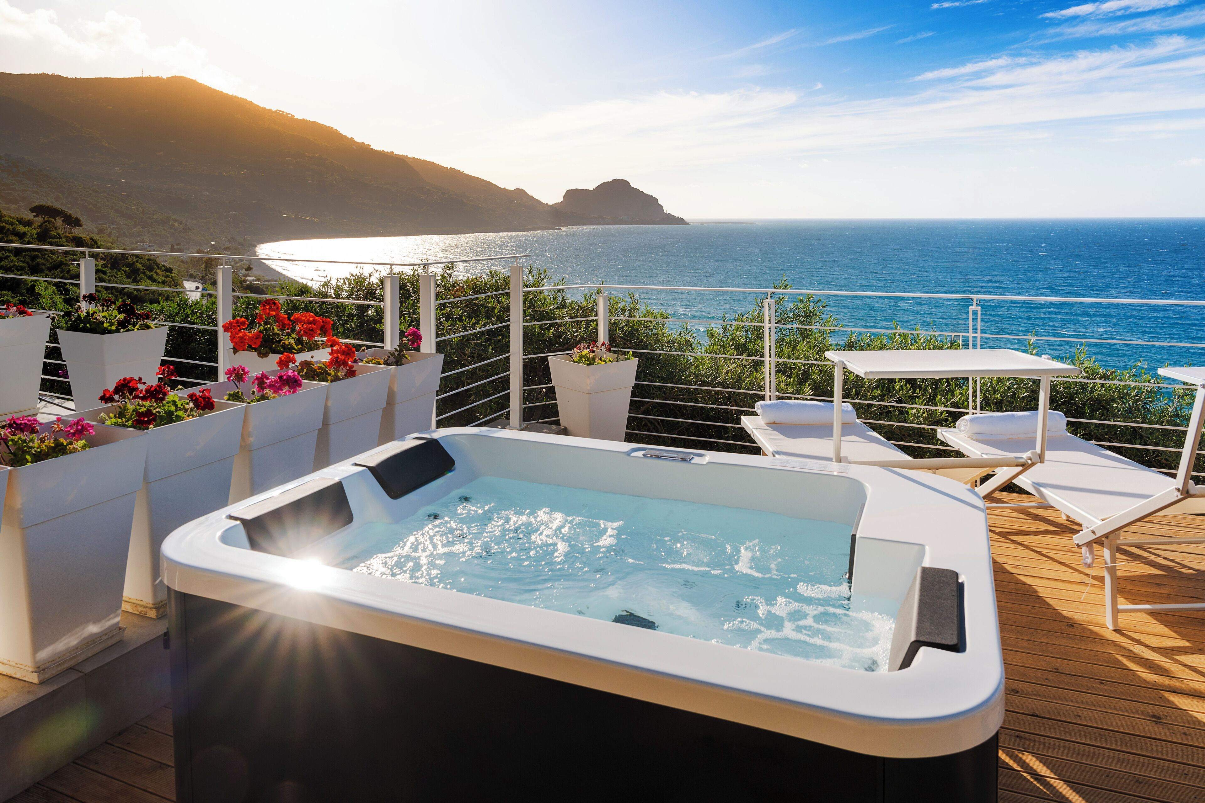 A hot tub on a wooden deck with a view of the ocean and hills.