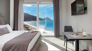 A hotel room with a bed, a table with a magazine, a cup, and a view of the ocean and mountains. - Emerald Boutique Hotel (Cefalù)