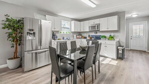 A modern kitchen with white cabinets, stainless steel appliances, a dining table with chairs, and a potted plant. - Hollywood of the south 3bed 2bath, Short walk to the square (Covington)