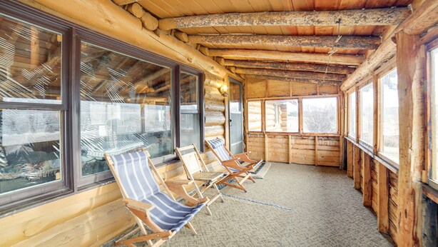 A log cabin with wooden walls and ceiling, large windows, and several striped lounge chairs. - Yellowstone Cabin Getaway Near National Park (Cameron)