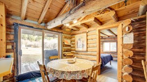A log cabin interior with a round dining table, wooden chairs, a bed, and a large window. - Yellowstone Cabin Getaway Near National Park (Cameron)
