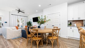 A modern living room with a round wooden table and chairs, a sofa, and a TV mounted on the wall.