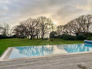 A swimming pool with a wooden deck, surrounded by a grassy lawn and trees.