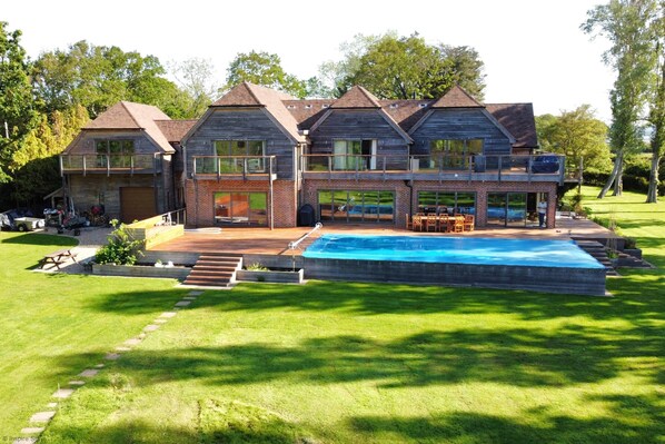 A large, modern house with a swimming pool, multiple decks, and a well-maintained lawn.