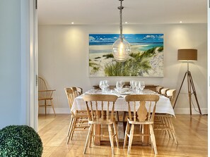 A dining area with a table set for six, surrounded by wooden chairs, a large painting of a beach scene, and a floor lamp.